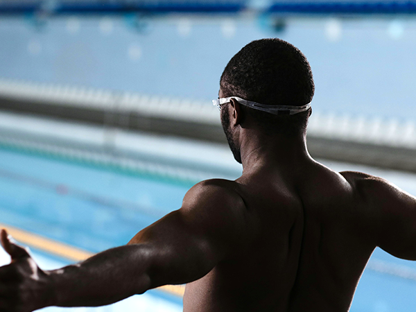 A Black swimmer with arms open facing the pool ready to dive